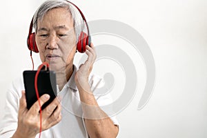 Asian senior woman in headphones listening to music online on mobile phone,old elderly hold smartphone wearing red headphones,
