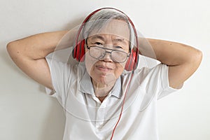 Asian senior woman in headphones listening to music online on mobile phone,old elderly wearing red headphones,relaxing free time,