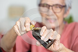 Asian senior woman hold a bottle of liquid drug,old elderly try to open the screw cap of bottle with difficulty,unscrew cap to