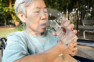 Asian senior woman holding glass of water,hands shaking while drinking water,elderly with hands tremor uncontrolled body tremors, photo