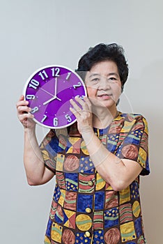 Asian senior woman holding purple clock in studio shot, specialt