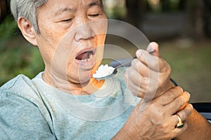 Asian senior woman holding spoon and hands tremor while eating rice,cause of hands shaking include parkinson`s disease,stroke, photo