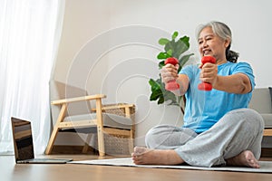 Asian senior woman lifting dumbbell for exercise and workout at home. Active mature woman doing stretching exercise in living room