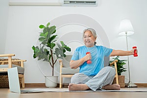 Asian senior woman lifting dumbbell for exercise and workout at home. Active mature woman doing stretching exercise in living room