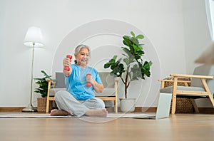 Asian senior woman lifting dumbbell for exercise and workout at home. Active mature woman doing stretching exercise in living room