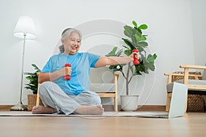 Asian senior woman lifting dumbbell for exercise and workout at home. Active mature woman doing stretching exercise in living room
