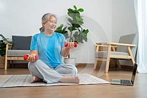 Asian senior woman lifting dumbbell for exercise and workout at home. Active mature woman doing stretching exercise in living room