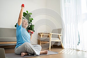 Asian senior woman lifting dumbbell for exercise and workout at home. Active mature woman doing stretching exercise in living room