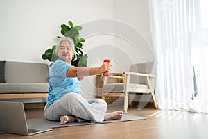 Asian senior woman lifting dumbbell for exercise and workout at home. Active mature woman doing stretching exercise in living room