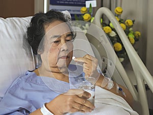 Asian senior woman lying in hospital bed, taking medicine. Elderly health concept
