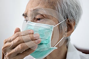 Asian senior woman in a medical mask,elderly patient covering nose and mouth with her hand while coughing or sneezing,prevent the