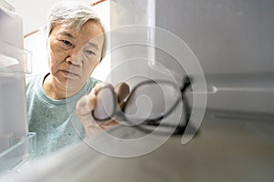 Asian senior woman with memory impairment symptoms,forget her glasses in the refrigerator or storing glasses in the fridge,female photo