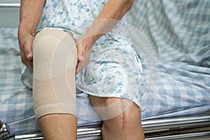 Asian senior woman patient with bandage compression knee brace support injury on the bed in hospital ward, healthy strong medical