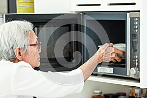 Asian senior woman putting bowl in microwave oven to reheat the leftovers,old elderly heating overnight food in kitchen,