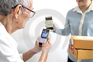 Asian senior woman receiving parcel post box from delivery service,paying deliver with smartphone to scan QR code payment purchase