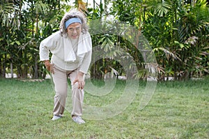 Asian Senior woman sitting or flop falling in garden park and having knee pain. kneel Arthritis pain concept. old female suffering