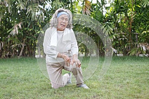 Asian Senior woman sitting or flop falling in garden park and having knee pain. kneel Arthritis pain concept. old female suffering