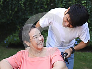 Asian senior woman sitting on wheelchair with her son in the garden