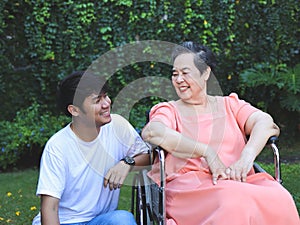 Asian senior woman sitting on wheelchair with her son in the garden