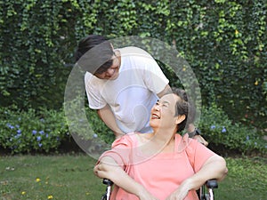 Asian senior woman sitting on wheelchair with her son in the garden