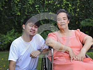 Asian senior woman sitting on wheelchair with her son in the garden