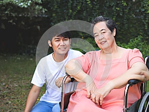 Asian senior woman sitting on wheelchair with her son in the garden