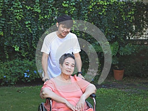 Asian senior woman sitting on wheelchair with her son in the garden