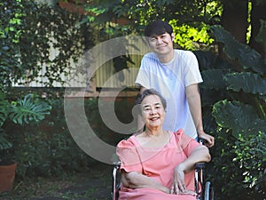 Asian senior woman sitting on wheelchair with her son in the garden