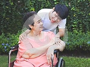 Asian senior woman sitting on wheelchair with her son in the garden