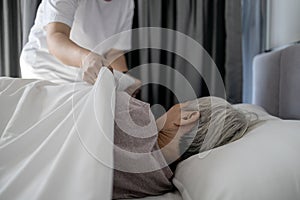 Asian senior woman is sleeping on a bed in bedroom,female caregiver cover senior patient with blanket,assisting old people,putting