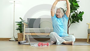 Asian senior woman stretching for exercise and workout at home. Active mature woman doing stretching exercise in living room.