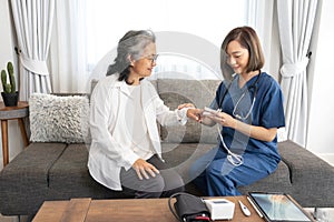 asian senior woman talking with a home visiting nurse,young female nurse measuring pulse with oximeter
