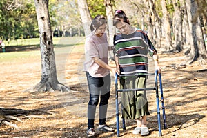 Asian senior woman use walking aid during rehabilitation after knee surgery, young carer assisting reassuring mature elderly