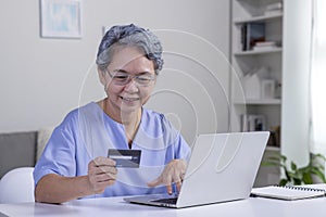 Asian senior woman using Laptop and credit card payment shopping online with customer network connection