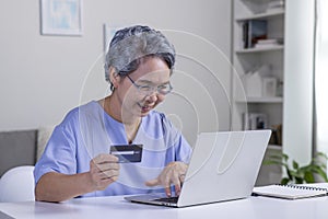 Asian senior woman using Laptop and credit card payment shopping online with customer network connection via omni channel system.