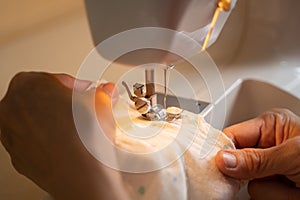 Asian senior woman using sewing machine making baby clothes at home.