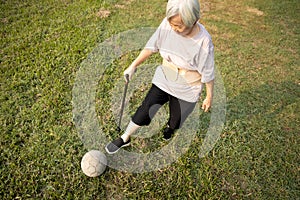 Asian senior woman with walking stick,playing with old football,healthy female elderly is kicking soccer ball,physical exercise,