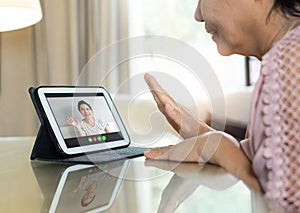 Asian Senior woman waving hand and talking to her relatives and family via internet and wireless technology. Old female making