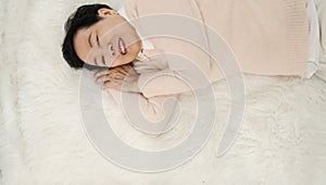 Asian senior woman wear pink sweater sleep on white fur bed