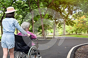 Asian senior woman in wheelchair with little child girl supporting disabled grandparent on walking green nature,grandmother and