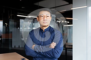 Asian serious and thinking man inside office looking out the window, businessman with crossed arms in shirt and