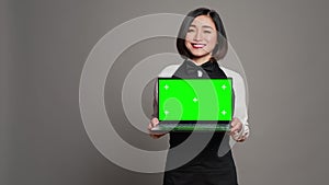 Asian server presenting greenscreen display on laptop in studio