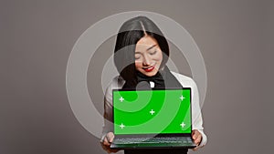 Asian server presenting greenscreen display on laptop in studio