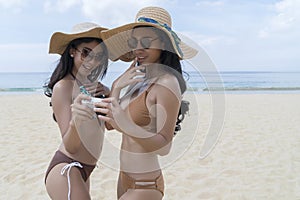 Asian Sexy young girls in bikini, enjoy wearing straw hat and sunglass, using camera and checking photo to camera together. Travel