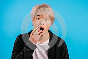 Asian shocked man afraid of something and looks into camera with big eyes full of horror over blue wall background