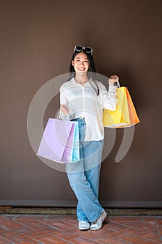 Asian shopaholic woman wearing sunglasses headband with many colorful shopping bags in both hands