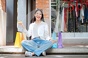 Asian shopaholic woman wearing sunglasses headband with many colorful shopping bags and holding credit card