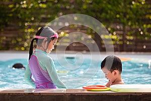 Asian sibling girl and boy playing water with toy together in the swimming pool with fun.