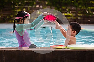 Asian sibling girl and boy playing water with toy together in the swimming pool with fun.