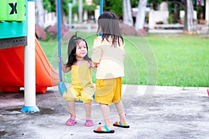 Asian sibling girl playing in the playground. The older sister stood talking to the sister sitting on the swing.